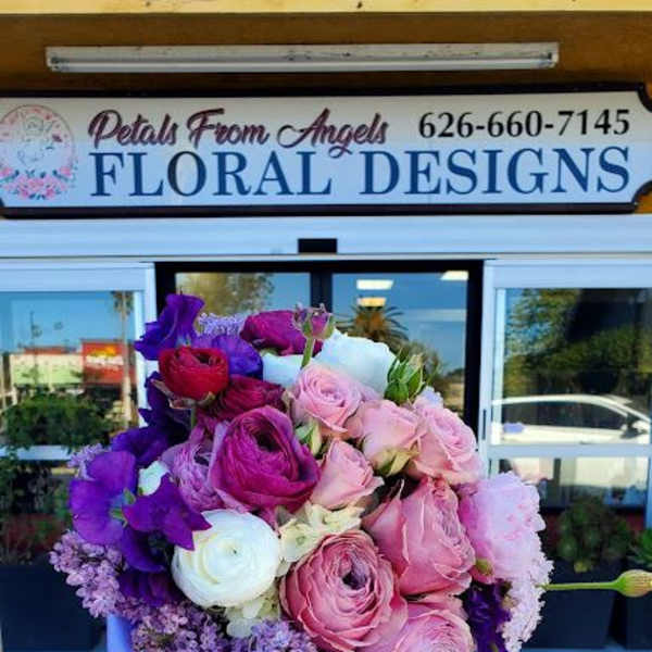 Hand-tied bouquet of pink roses, purple blooms, and white ranunculus with lavender ribbons.