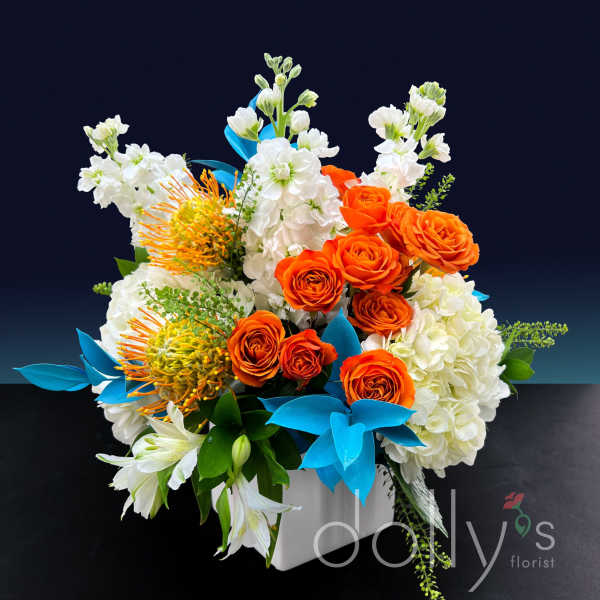 Orange roses and white flowers arranged in a white box with blue accents