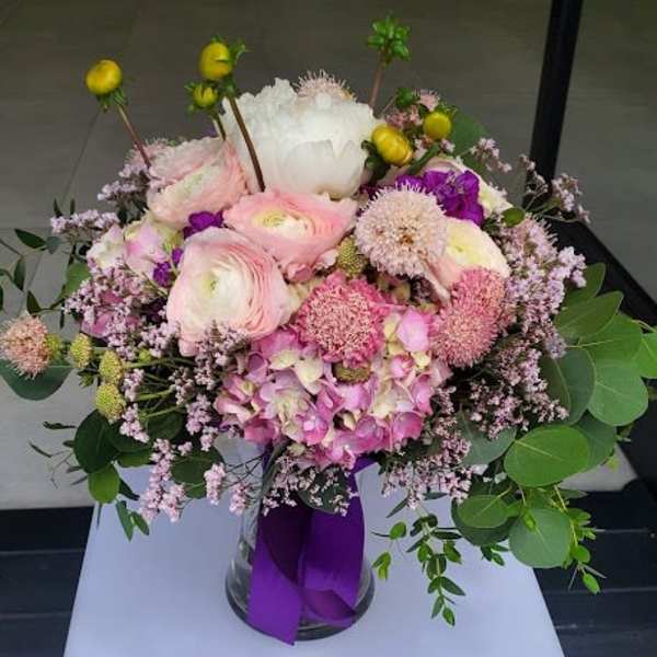 Round arrangement of pink and white mixed flowers in a glass vase with a purple ribbon