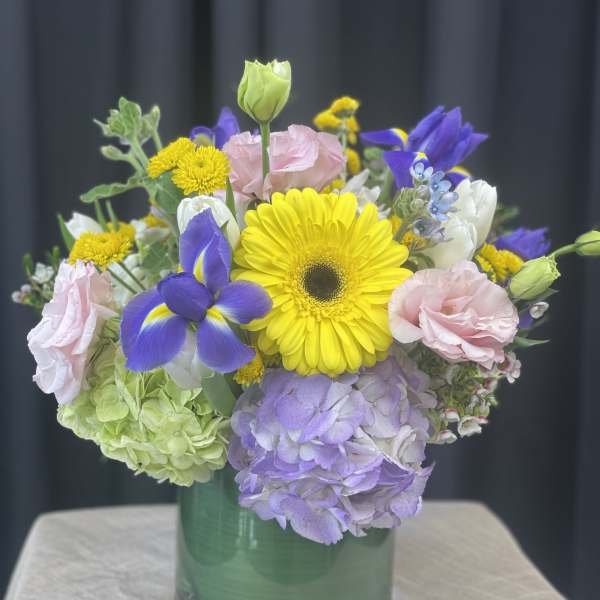 Mixed bouquet in a green glass vase with yellow, purple, pink, and white blooms