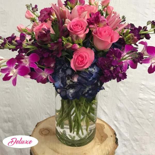 Pink roses and purple flowers arranged in a clear glass vase