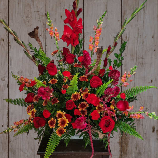 Large red floral arrangement with roses and tall gladiolus in a black container