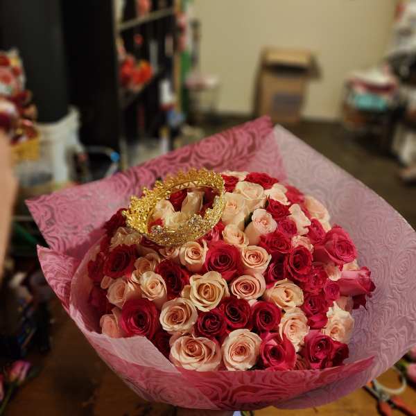 Bouquet of red and blush roses wrapped in pink paper with a gold crown