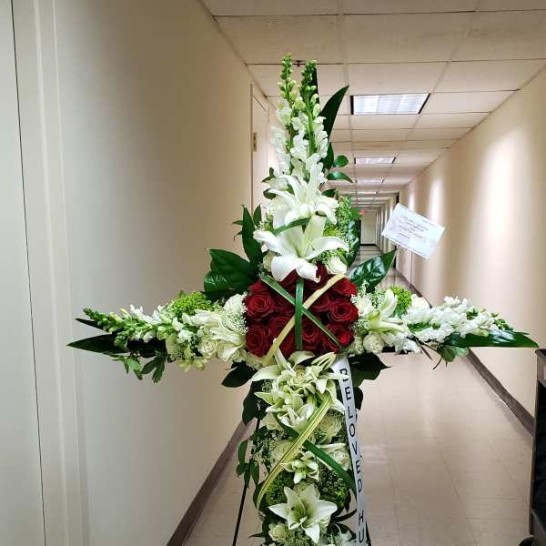 Tall cross-shaped funeral spray with white lilies, snapdragons, and red roses on a metal easel
