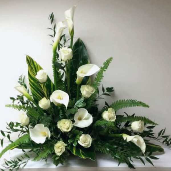 White calla lilies and roses arranged with large glossy leaves in a low, fan-shaped display