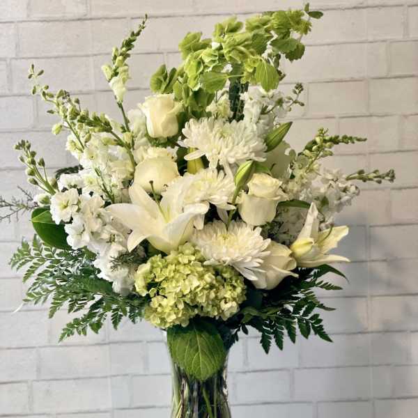 White floral arrangement in a clear glass vase with lilies, roses, and chrysanthemums
