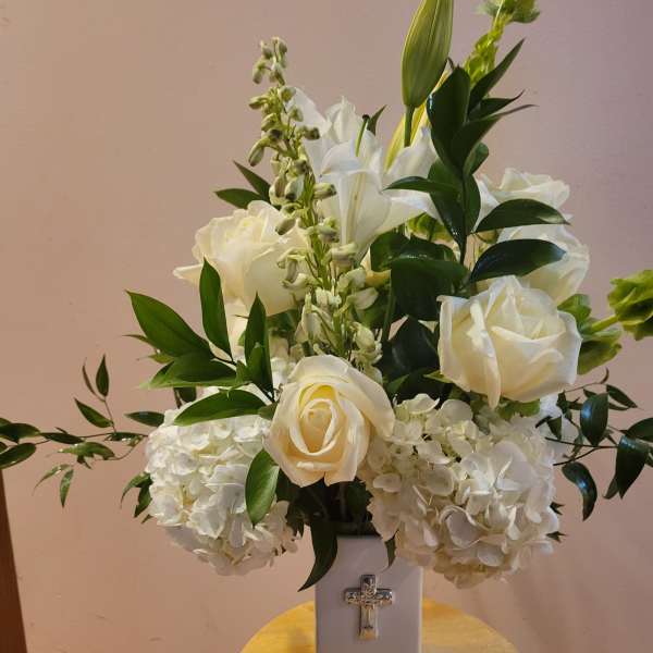 White roses and hydrangeas in a tall vase with a cross emblem