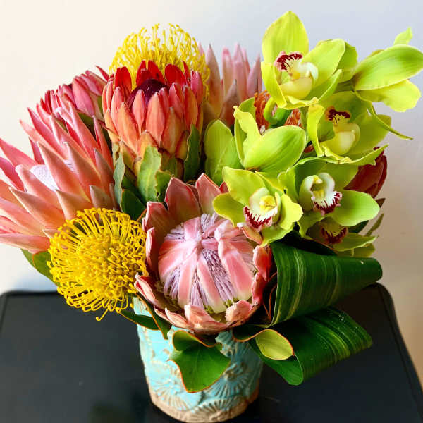 Bouquet of pink protea and green orchids in a blue vase