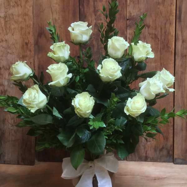 White roses arranged in a glass vase with a white ribbon