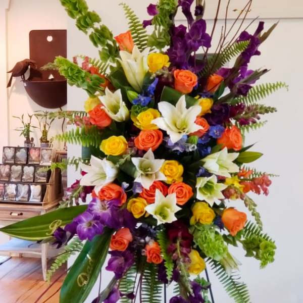 Tall standing spray of mixed roses, lilies, and purple flowers on an easel