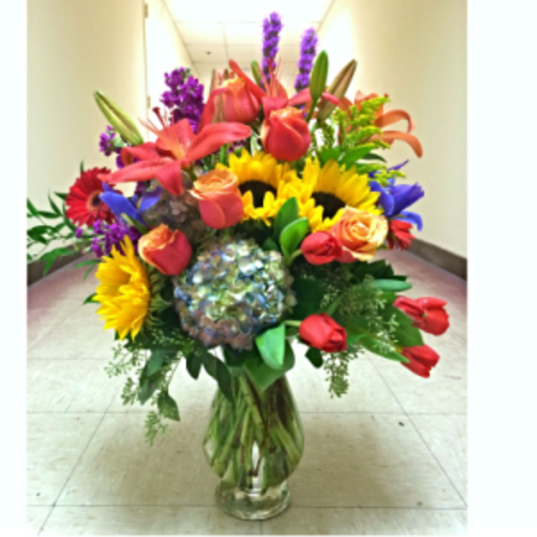 Colorful mixed bouquet in a clear glass vase with sunflowers and roses