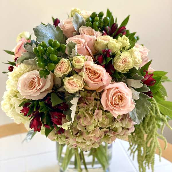 Round arrangement of blush roses, hydrangeas, and red flowers in a clear glass vase