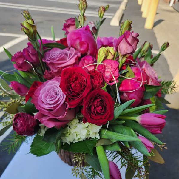 Round arrangement of red and pink roses and tulips in a rustic container