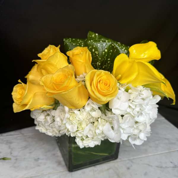 Yellow roses and white hydrangeas in a square glass vase