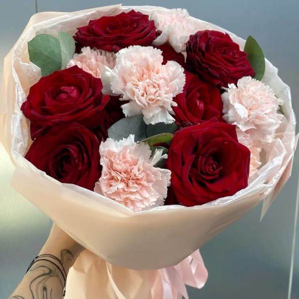 Bouquet of red roses and pale pink carnations wrapped in cream paper
