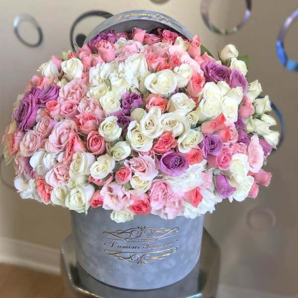 Large arrangement of pink, white, and lavender roses in a gray hatbox.