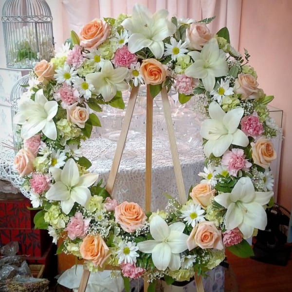 Large floral wreath with white lilies, peach roses, and pink accents on an easel