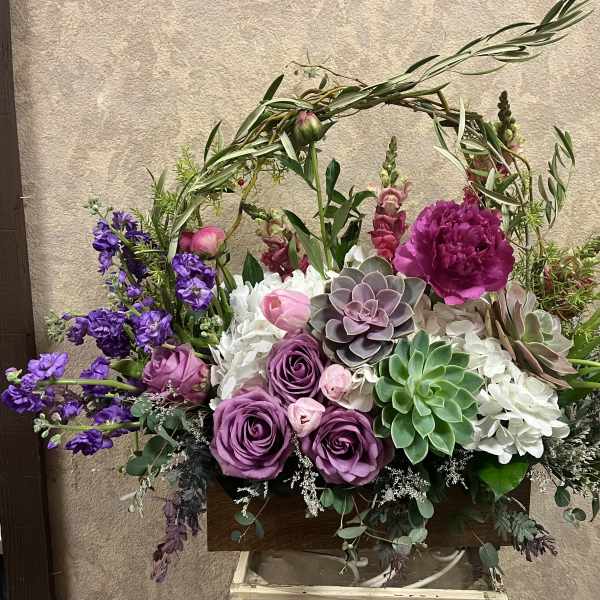 Garden-style arrangement of purple roses, succulents and white hydrangeas in a wooden box.
