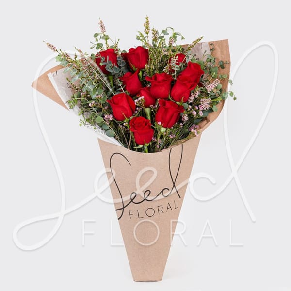 Bouquet of red roses with small pink filler flowers wrapped in a kraft paper cone sleeve