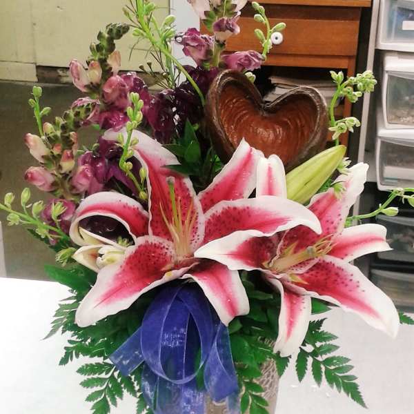 Pink stargazer lilies in a vase with a purple ribbon and heart-shaped accent