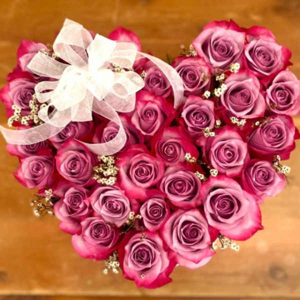 Heart-shaped bouquet of pink and purple roses with a white ribbon bow