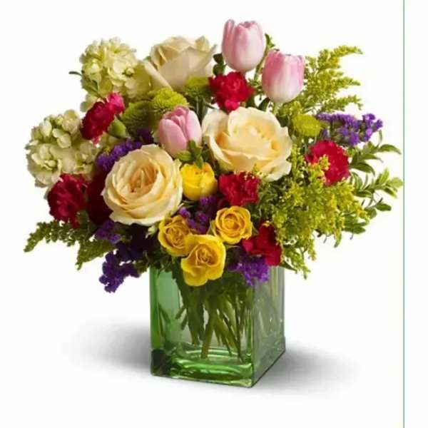 Mixed bouquet of yellow and cream roses, pink tulips, and red carnations in a green glass cube vase