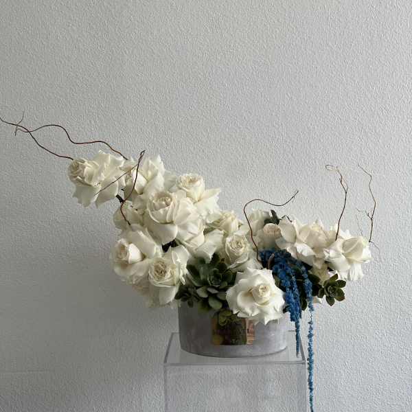 White rose arrangement with blue hanging accents in a gray container