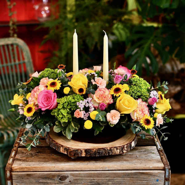 Colorful floral centerpiece with two tall white candles in a wood slice base