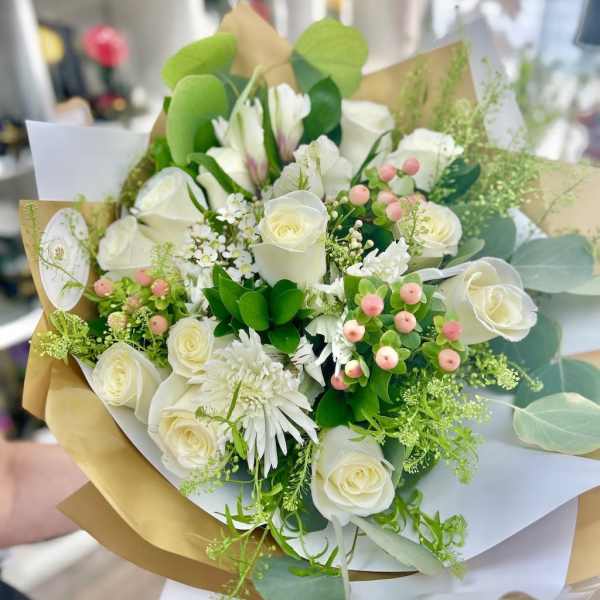 Hand-tied bouquet of white roses and mixed white flowers with pink berries in kraft and white wrap
