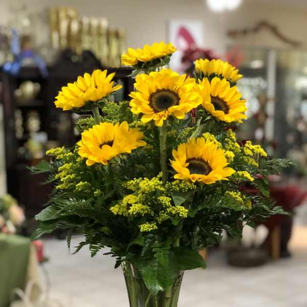 Tall clear vase of yellow sunflowers with small yellow filler flowers