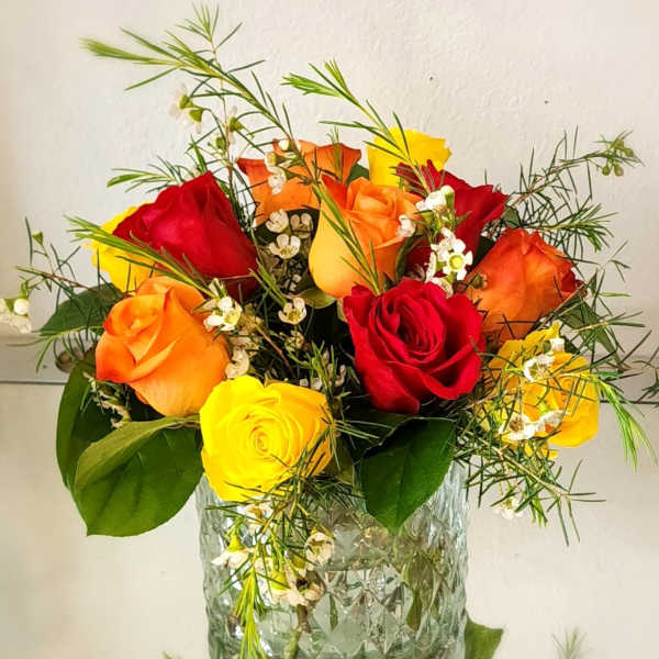 Bouquet of red, orange, and yellow roses in a clear glass vase
