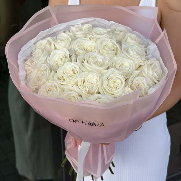 Large round bouquet of white roses wrapped in pale pink paper, held by a person in a white dress