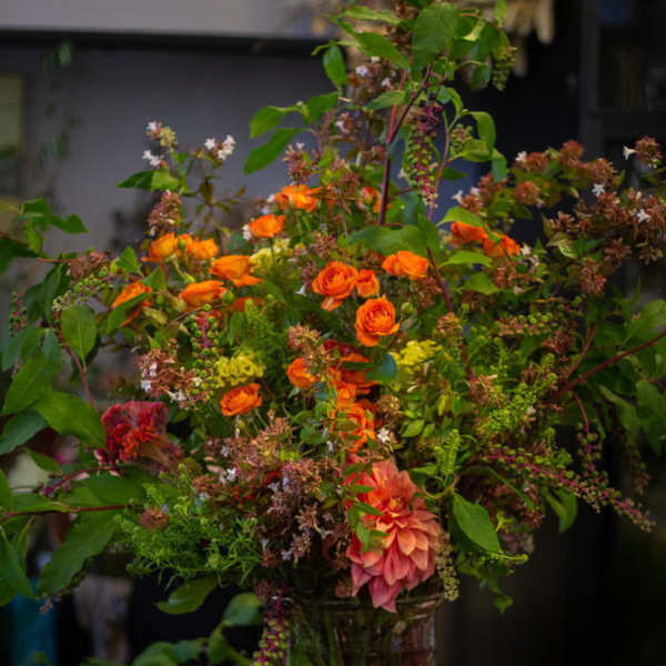 Tall mixed bouquet with orange roses and pink dahlias in a glass vase