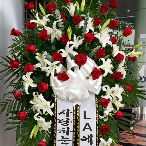 Large standing floral spray with red roses and white lilies, topped with a white bow