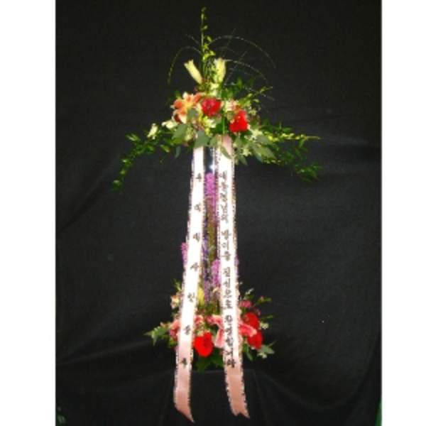 Tall two-tiered standing floral spray with red flowers and printed ribbons on a black background