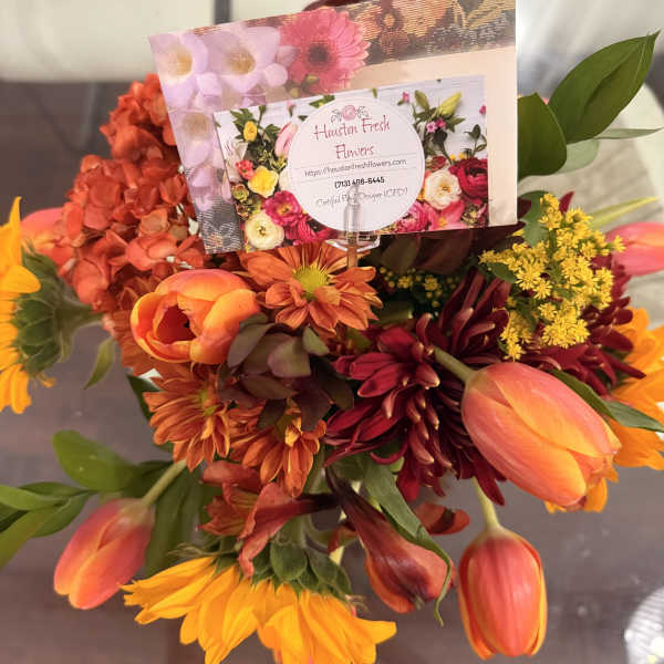 Bouquet of orange, yellow, and burgundy flowers with a florist card
