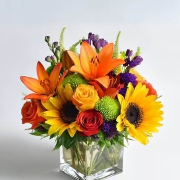 Colorful bouquet with sunflowers, roses, and lilies in a square glass vase