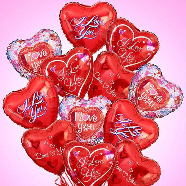Bundle of red heart-shaped I Love You balloons against a pink background