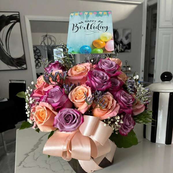 Bouquet of pink, peach, and lavender roses with a birthday card and ribbon