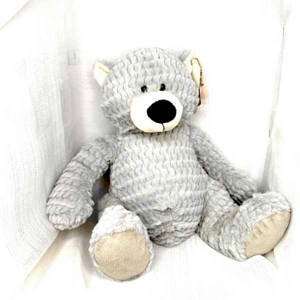 Gray plush teddy bear sitting against white fabric