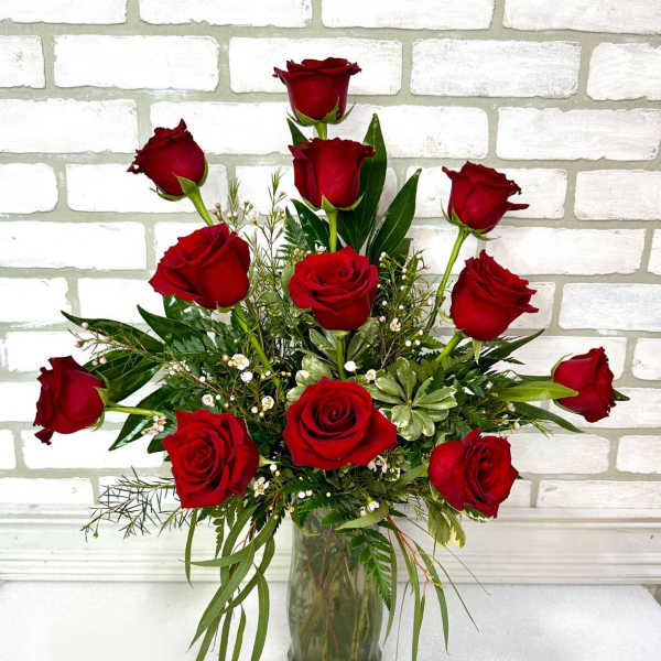 Red roses arranged in a clear glass vase with greenery