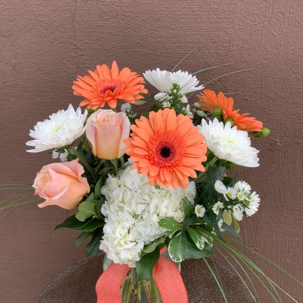 Bouquet of orange gerbera daisies, white mums, and peach roses in a glass vase