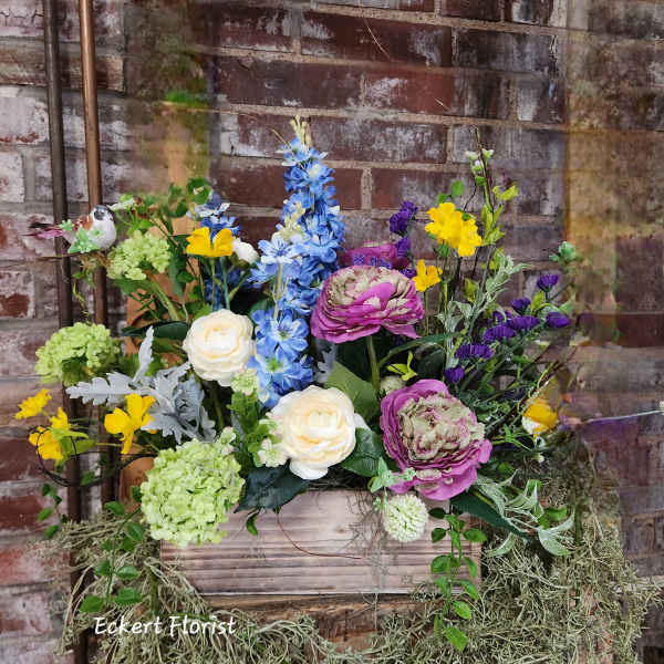 Mixed floral arrangement in a wooden box with blue, pink, yellow, and white blooms