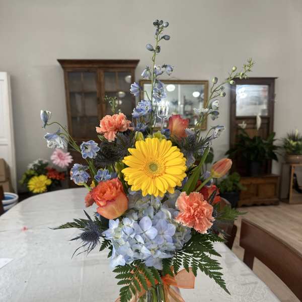 Mixed bouquet in a glass vase with yellow gerbera, blue hydrangea, and orange carnations