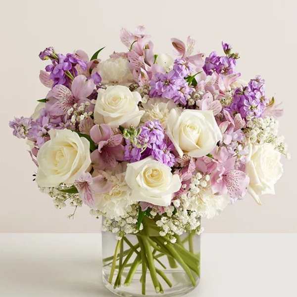 White roses and lavender flowers arranged in a clear glass vase