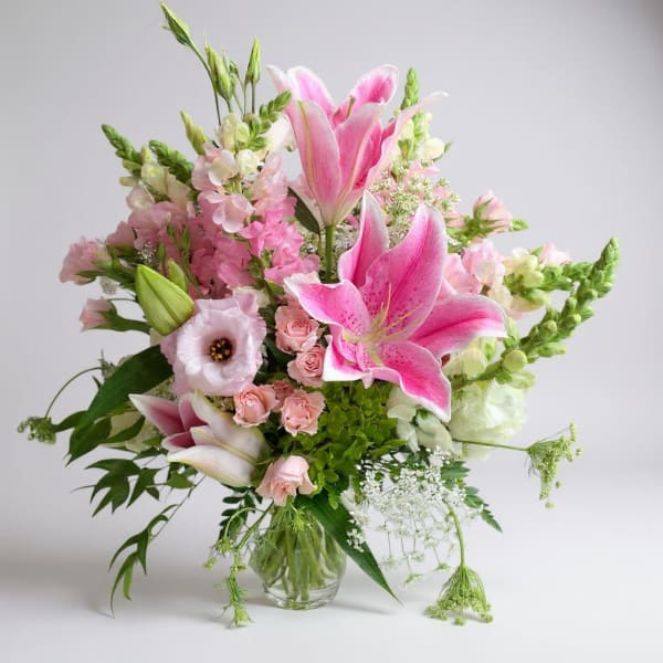 Tall pink and white arrangement with lilies, roses, and mixed blooms in a clear glass vase
