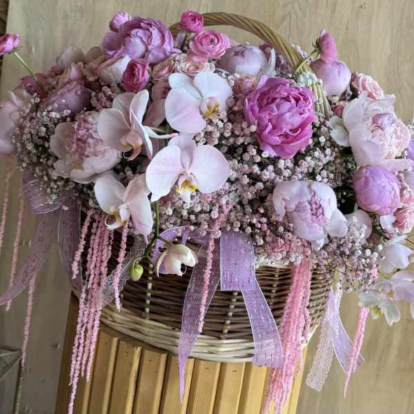 Pink floral arrangement in a wicker basket with orchids and peonies