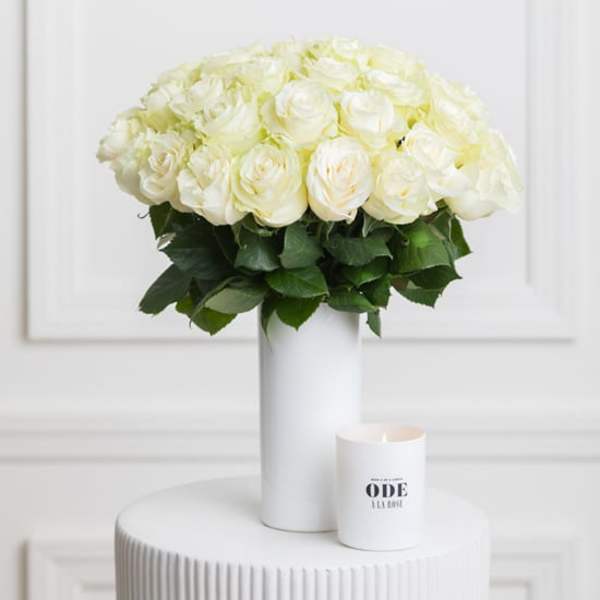 White rose bouquet in a tall white vase with a small candle beside it