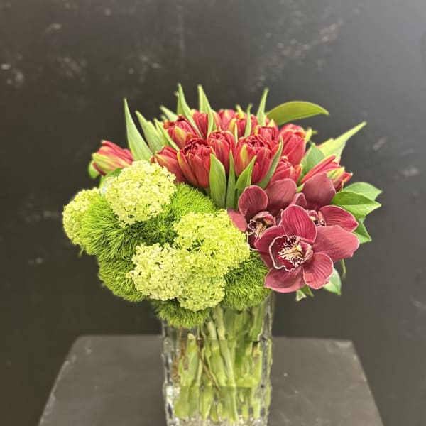 Bouquet of red tulips, green pom-pom blooms, and burgundy orchids in a glass vase