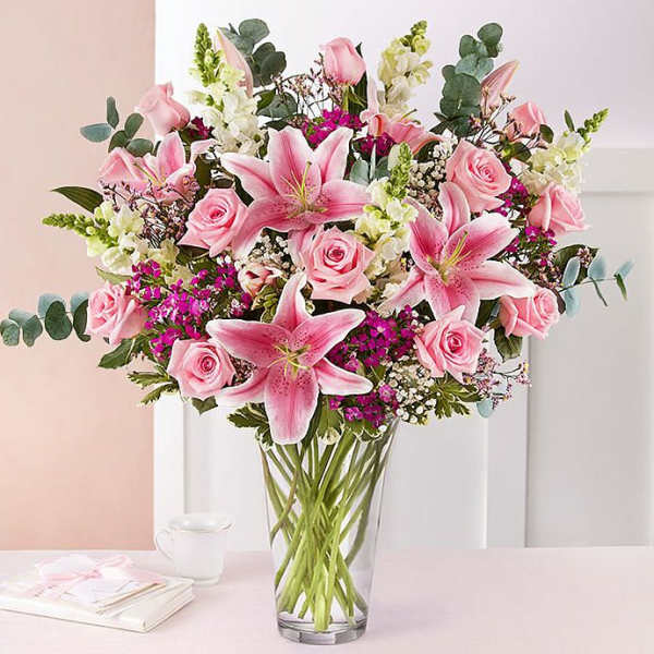 Tall mixed arrangement of pink lilies and roses with white flowers in a clear glass vase